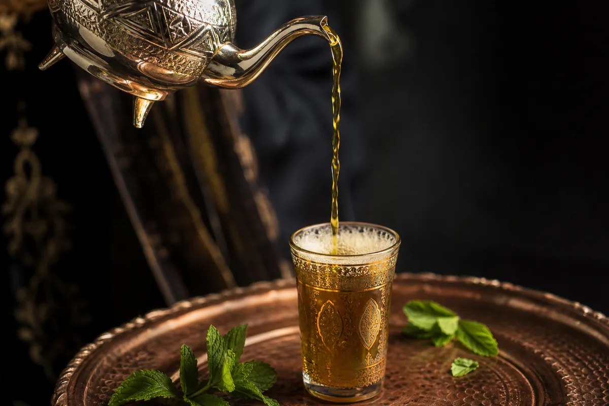Verre de thé à la menthe fumant servi de haut au-dessus d’un plateau en cuivre